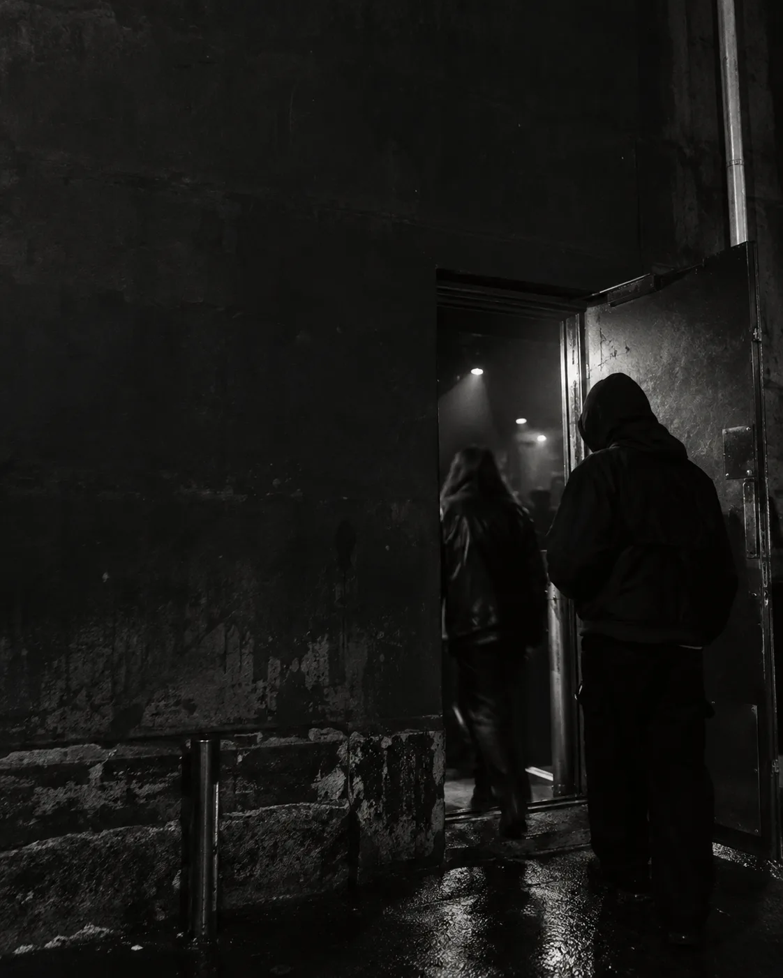 Black-and-white scene of people entering a dimly lit venue.